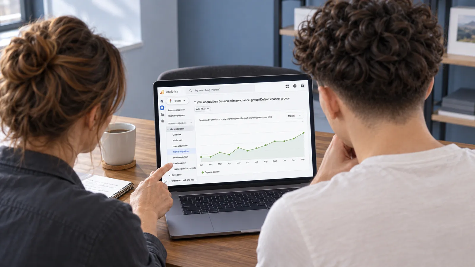 A business owner and search specialist, seen from behind, review an organic search traffic trend in GA4