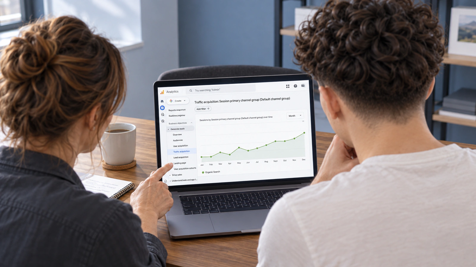 A business owner and search specialist, seen from behind, review an organic search traffic trend in GA4